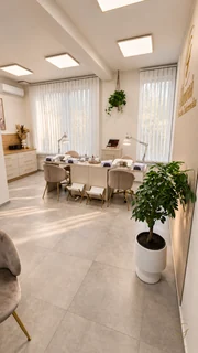 Stanowiska manicure i duża monstera w jasnym wnętrzu salonu.